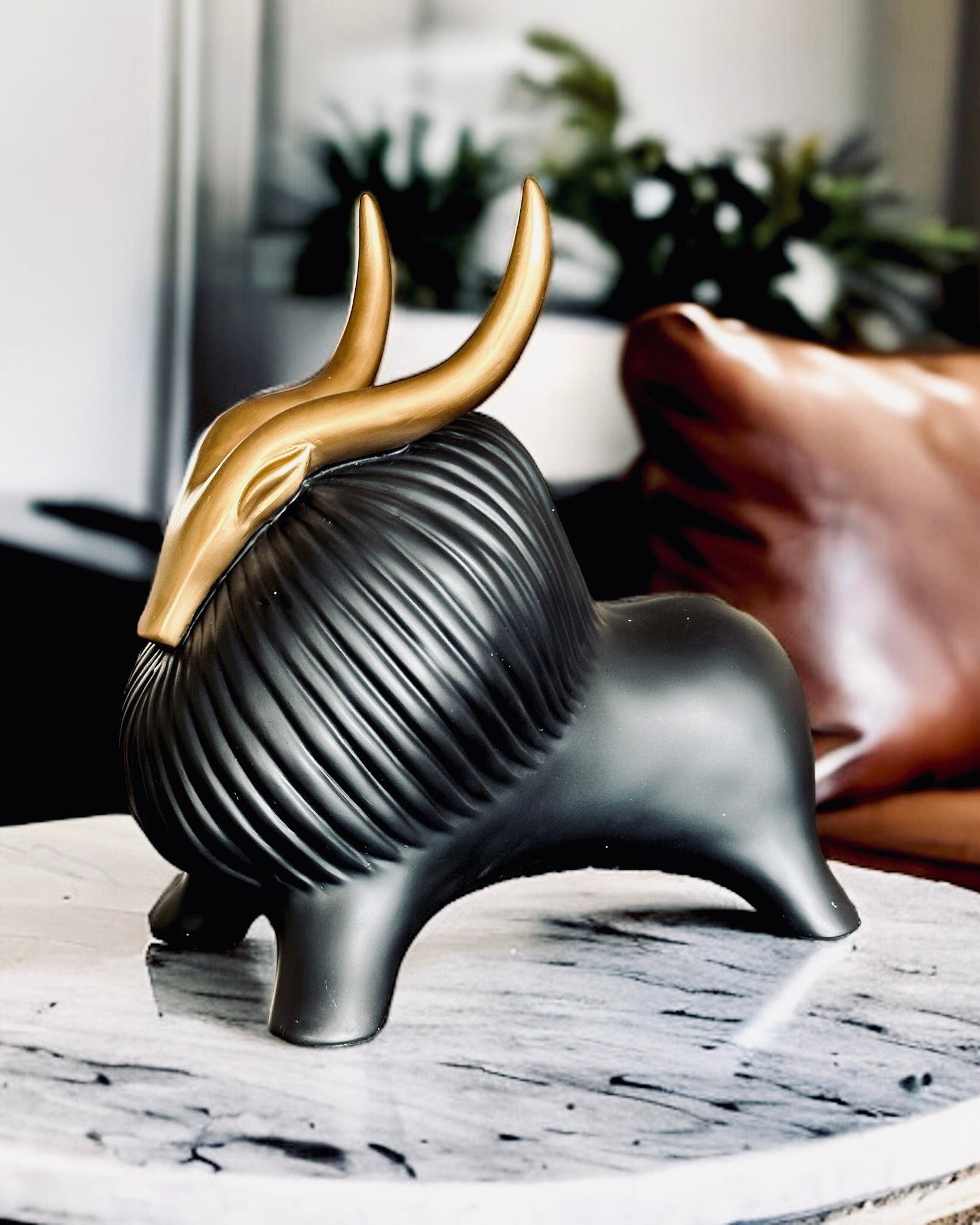 A black and gold resin figurine of a yak with horns, placed on a marble surface.