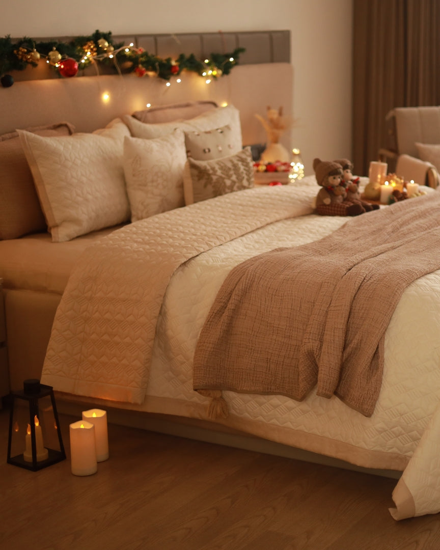 A bed with a beige and ivory reversible cotton bedspread, featuring a satin finish, with matching pillow covers on the bed in a decorated room.