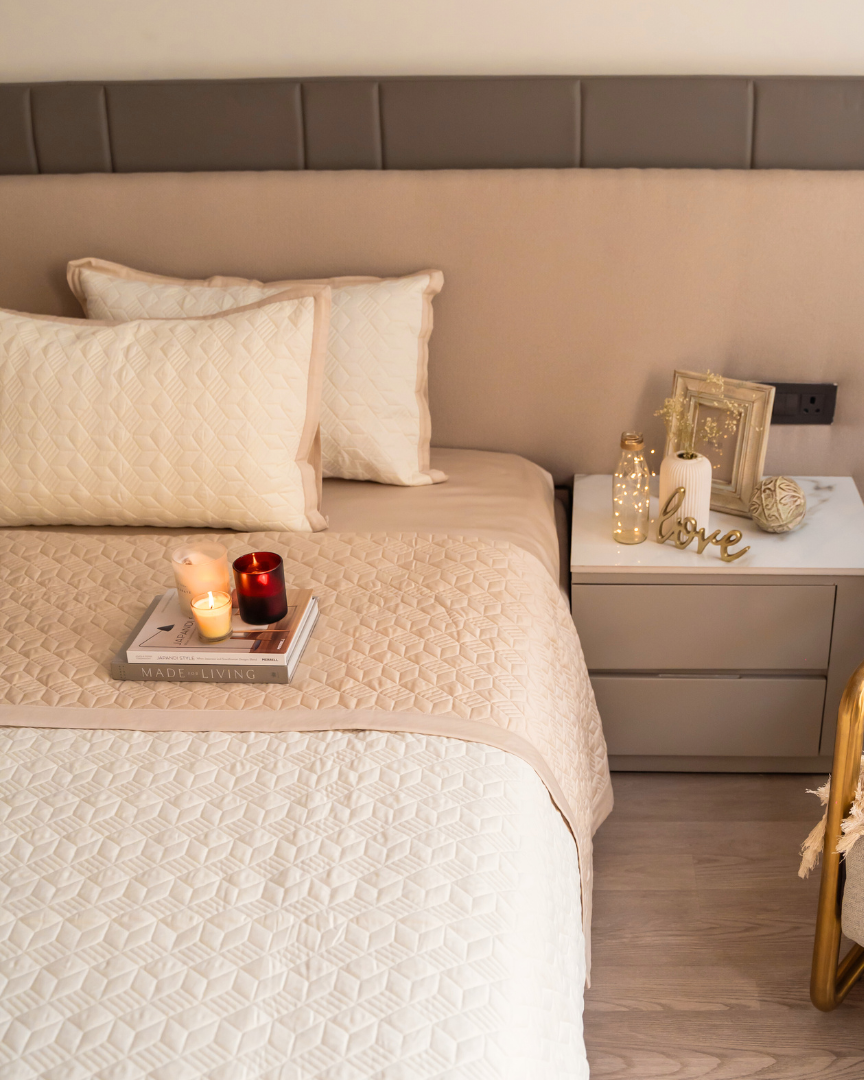 A beige and ivory cotton reversible bedspread on a bed with matching pillow covers, placed in a bedroom setting with decorative items on the bedside table.